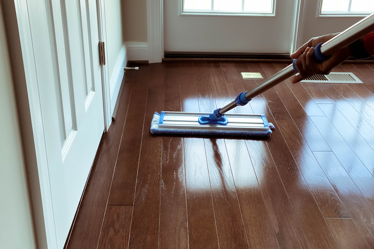 A person is using a dry mop to clean shiny dark hardwood flooring.