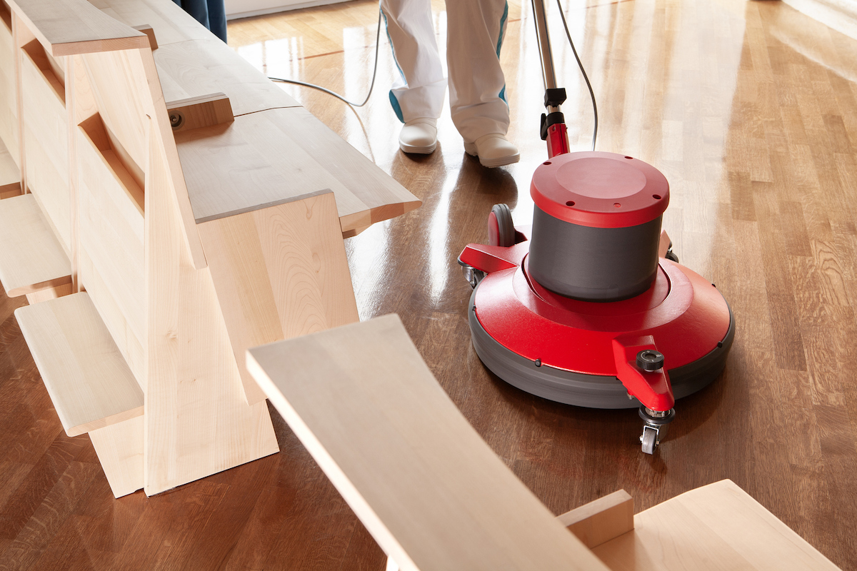 A person is using an electric floor buffer on a hardwood floor.