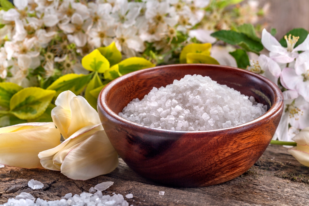 A wooden bowl of salt next to garden flowers.