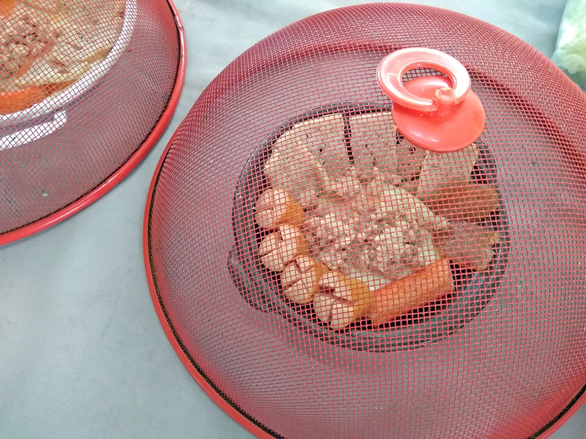 Red metal mesh domed covers over plates of food outdoors.