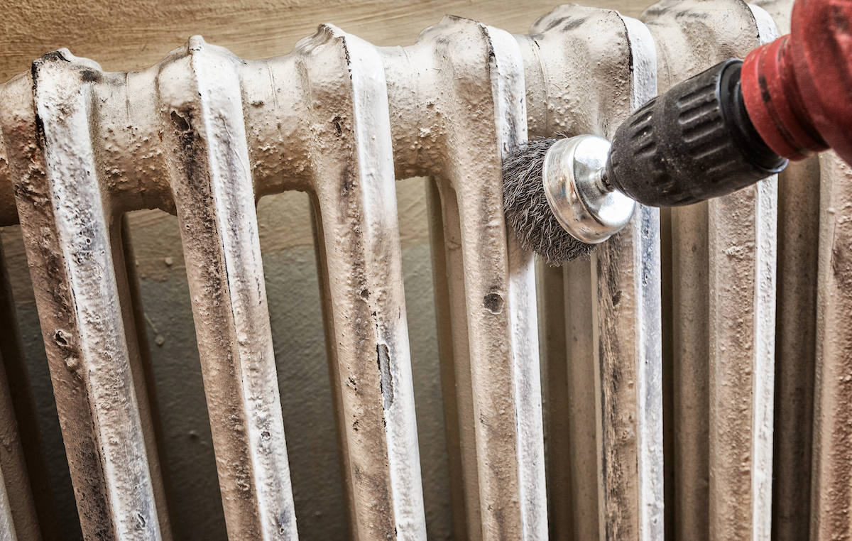 Person uses a wire brush attachment on a drill to sand a radiator.