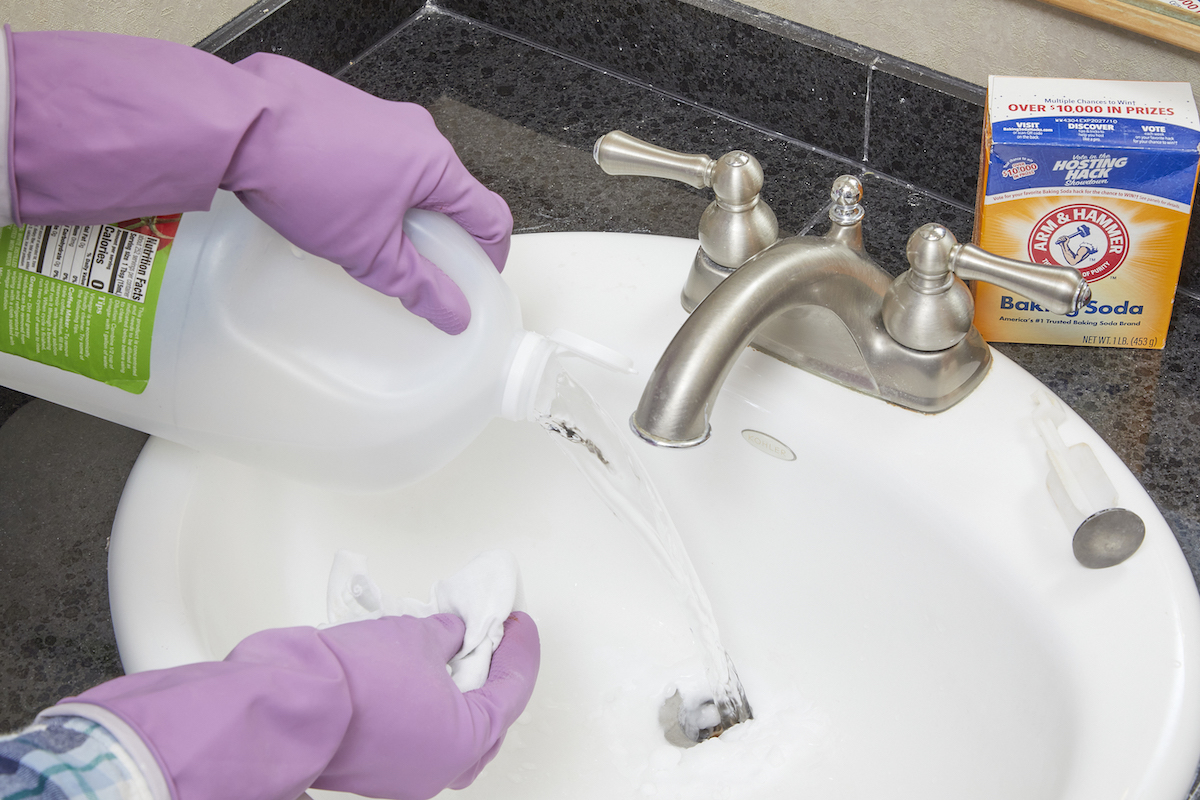 Woman pours vinegar and baking soda into a bathroom sink drain.