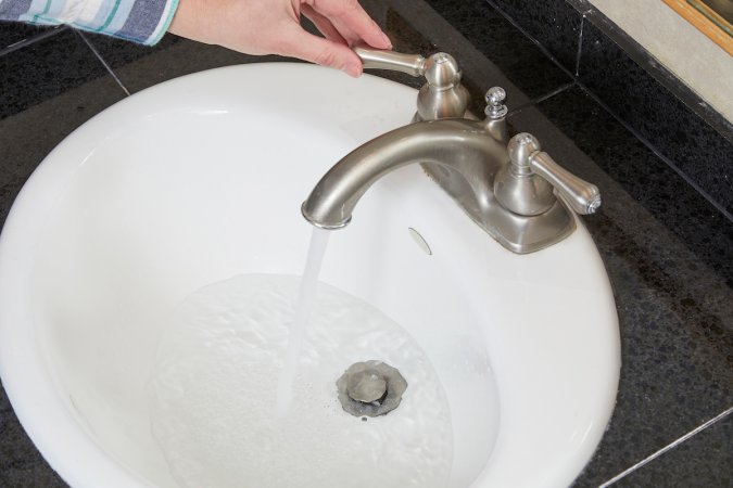 Woman turns the hot water handle on a sink with a slow drain.