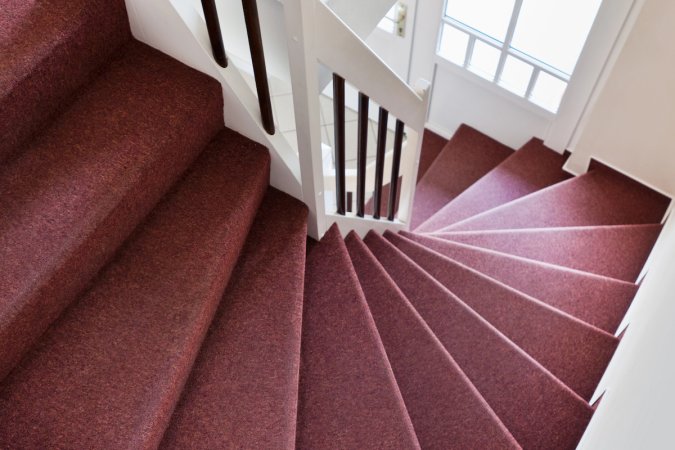 A maroon carpeted staircase with white banisters leads down to the first floor of a home.