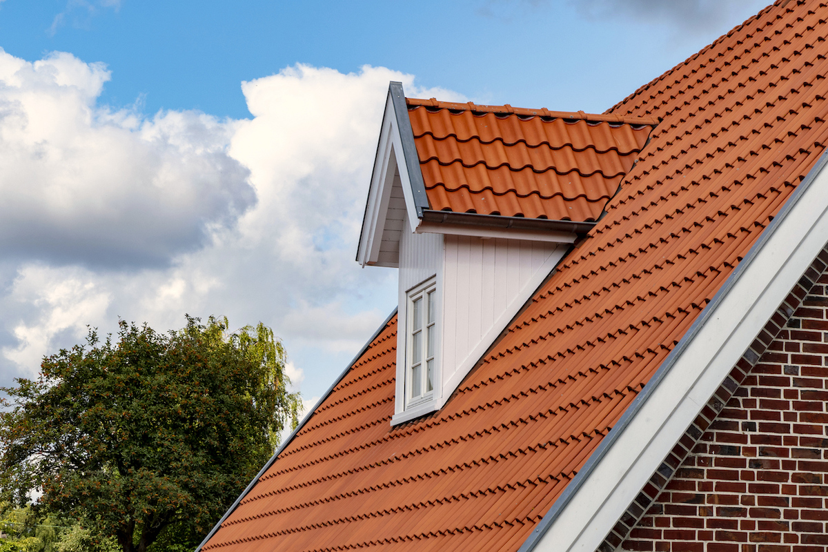 A brick home's roof features tiled shingles that are a Mediterranean-style terracotta color.