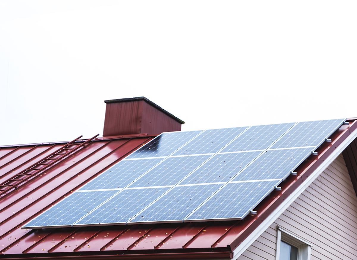 A solar panel is on a red metal roof of a house.