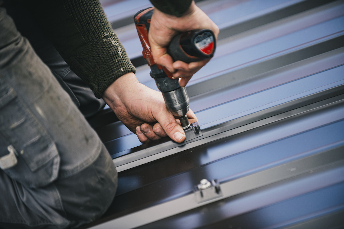 A person is using a tool to install metal roofing on a house.