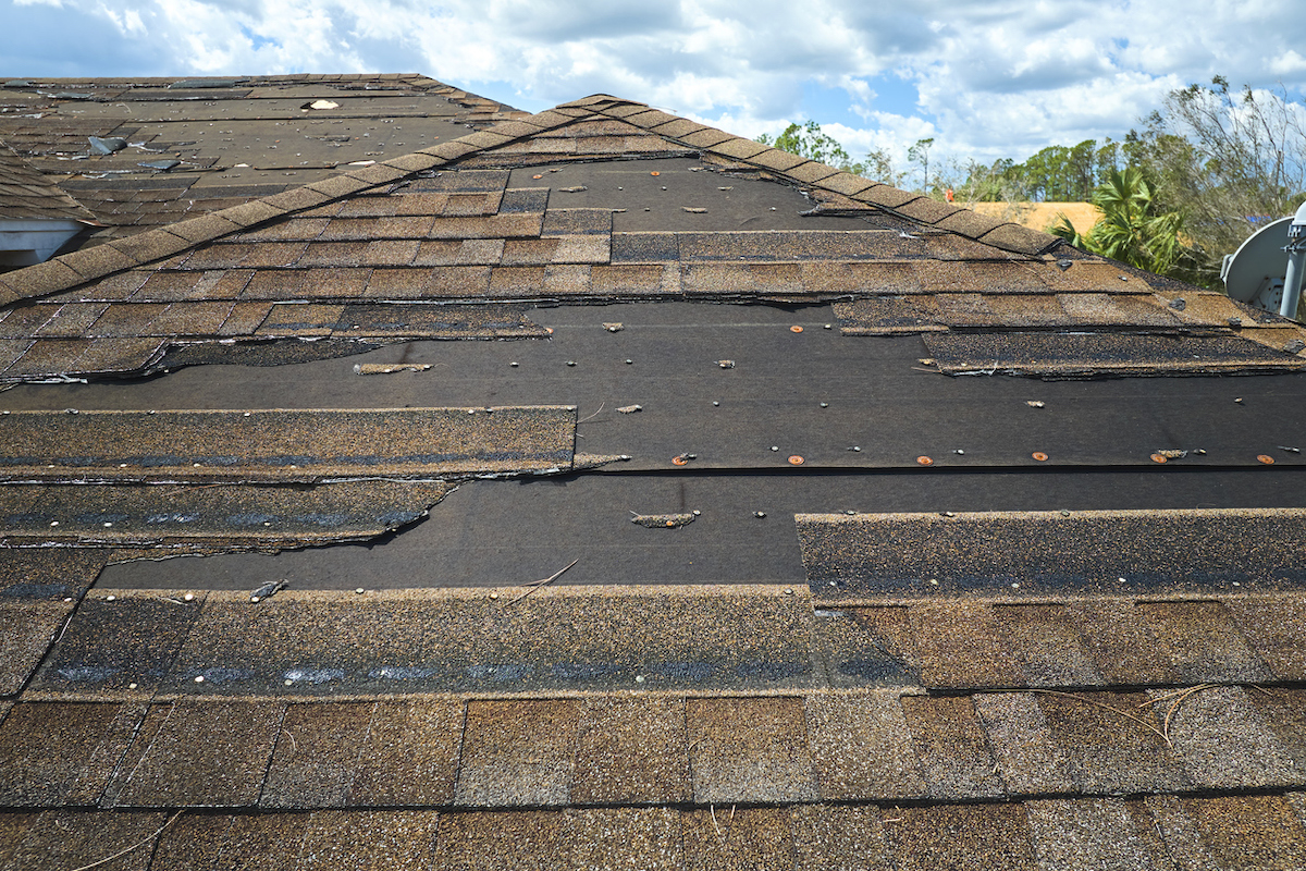 A damaged house's roof is missing shingles after a natural disaster.
