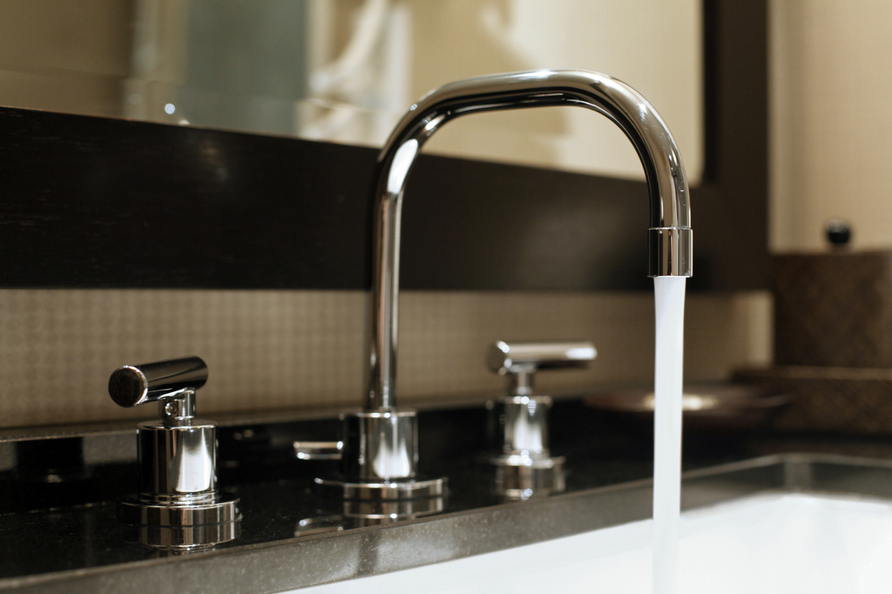 Water is running from a chrome faucet in a bathroom.