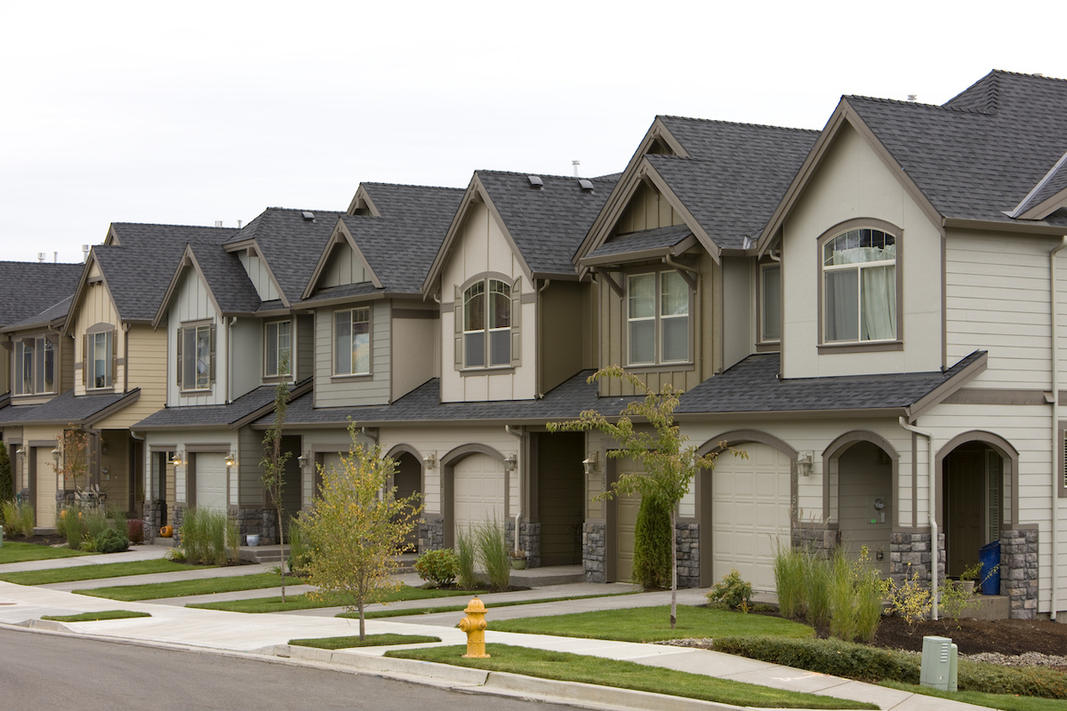 A row of similar-looking beige- and cream-colored homes have the same asphalt shingle roofing.