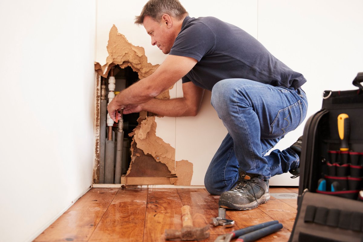 A person is repairing a burst pipe in a damaged wall.