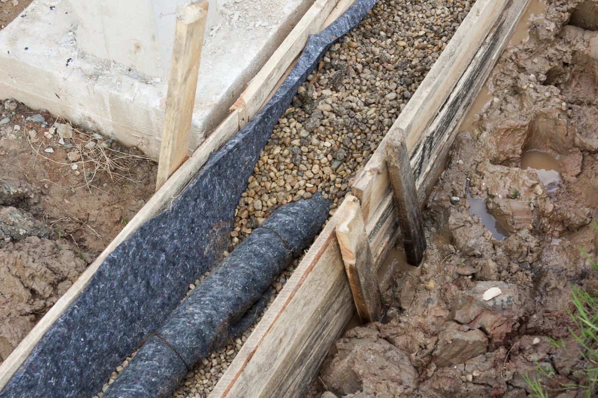 A French drain in the process of being covered by pebble stones.