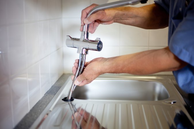 A professional kitchen fitter, in the process of completing the kitchen installation, fitting the new mixer Tap.