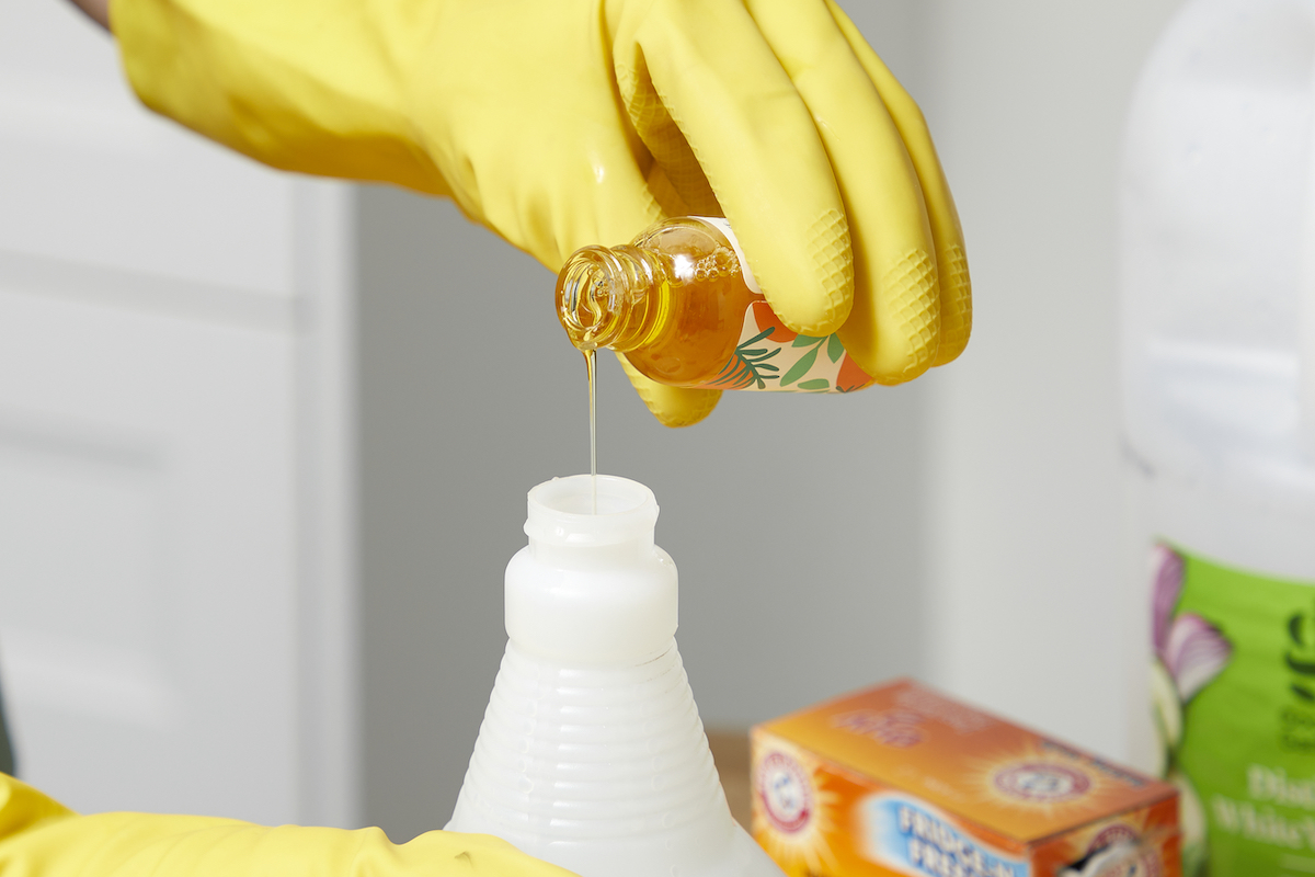 Woman wearing yellow rubber gloves adds essential oil to a spray bottle.