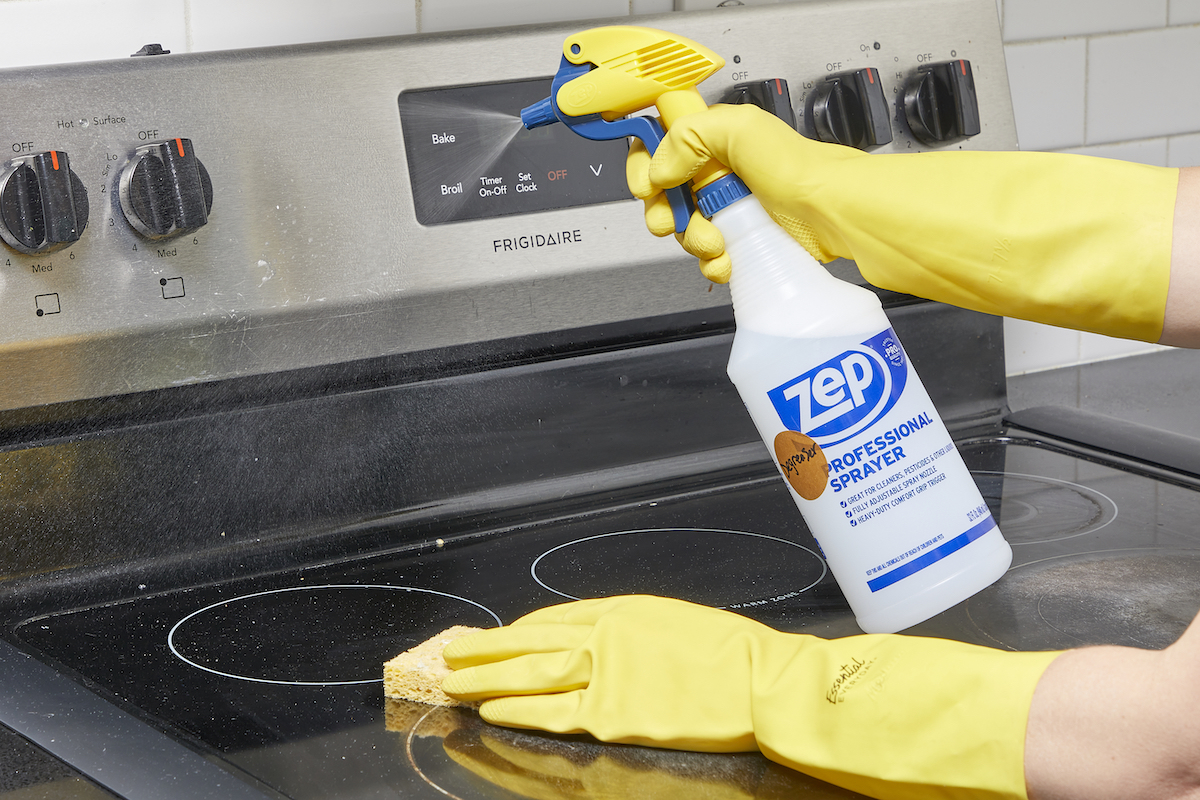 Woman wearing yellow cleaning gloves sprays homemade degreaser on a stove top.