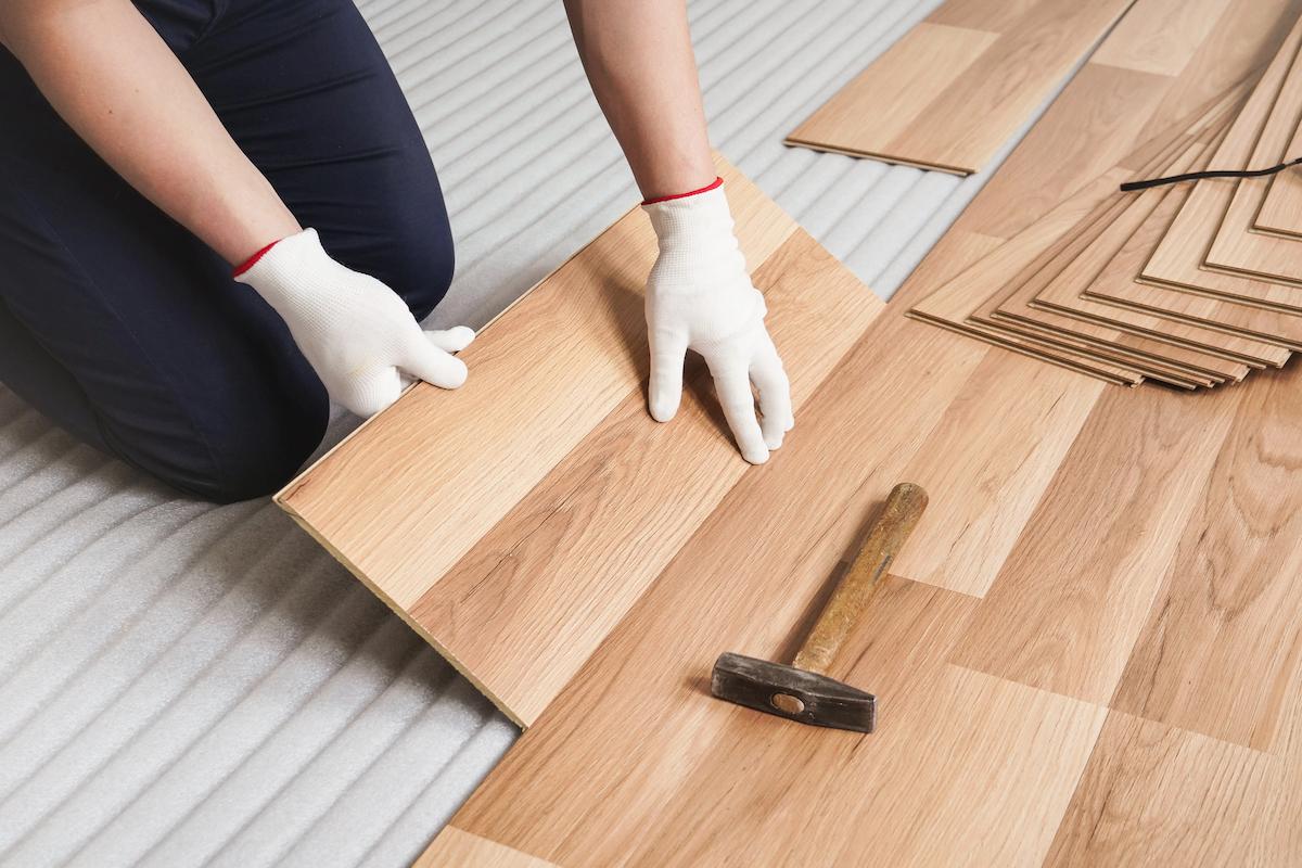 A person wearing white gloves is installing wooden laminate flooring.