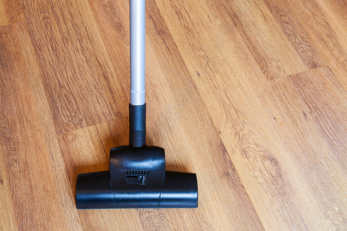 A black vacuum cleaner is being used to clean a wooden laminate floor.