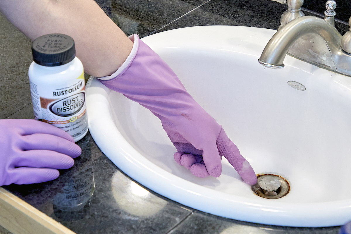 Woman wearing cleaning gloves uses naval jelly on rust in sink.