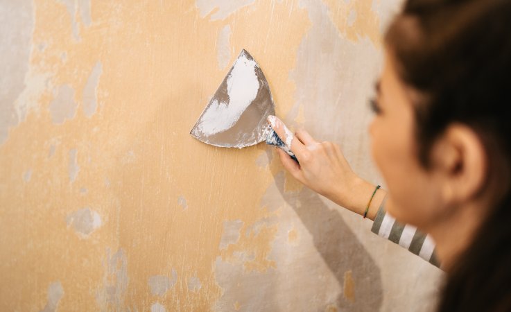 Rear view of a woman peeling paint from the wall.