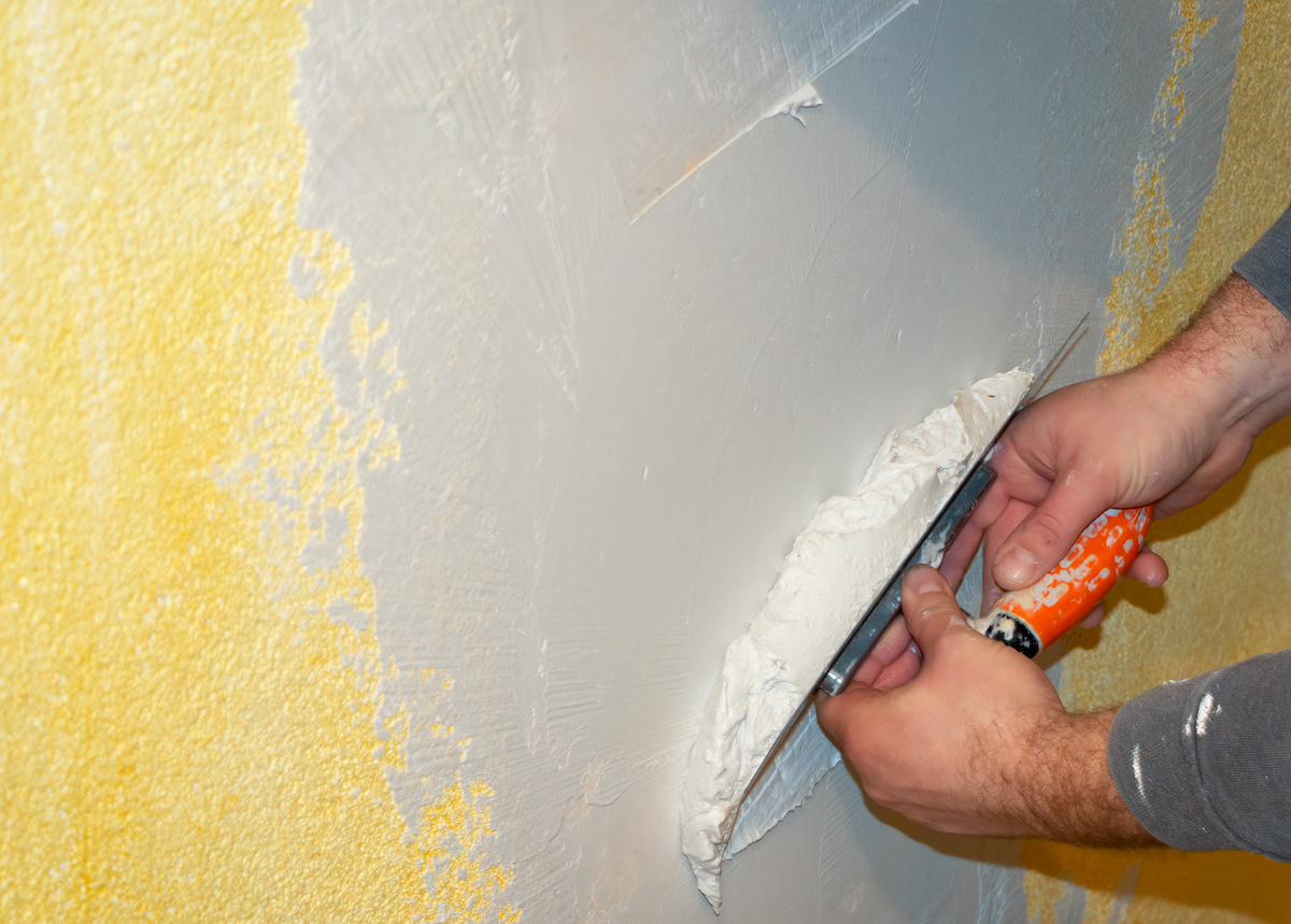 Skim coating a yellow painted wall.