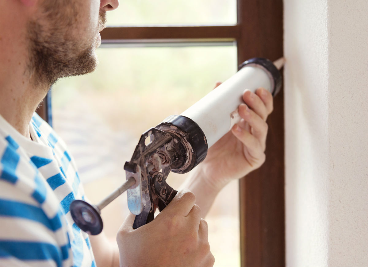 A man is caulking an interior window with a caulking gun.