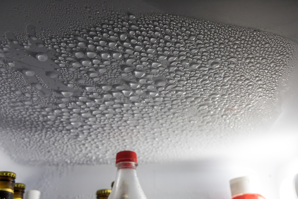 Condensation drops cling to the inside of a refrigerator above bottles.