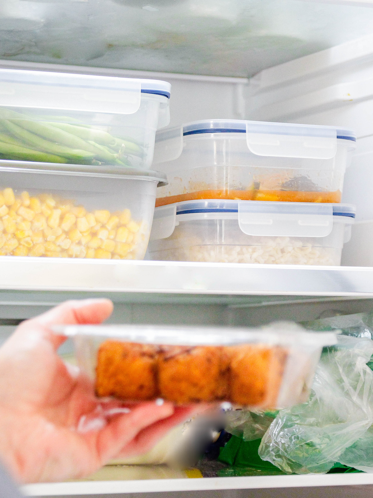 A person is putting food inside of matching locking food storage containers into a refrigerator.