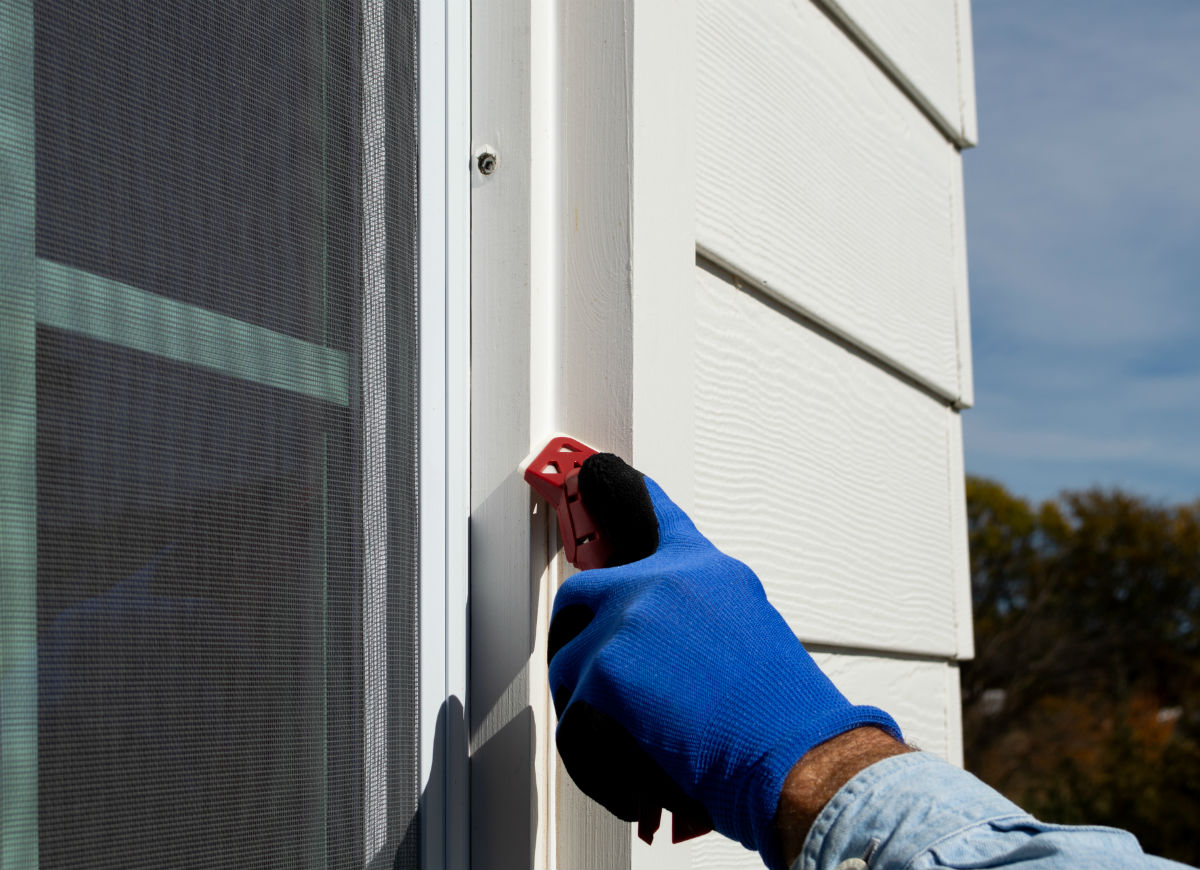 A person is using a caulk application tool to smooth caulk on an exterior window.