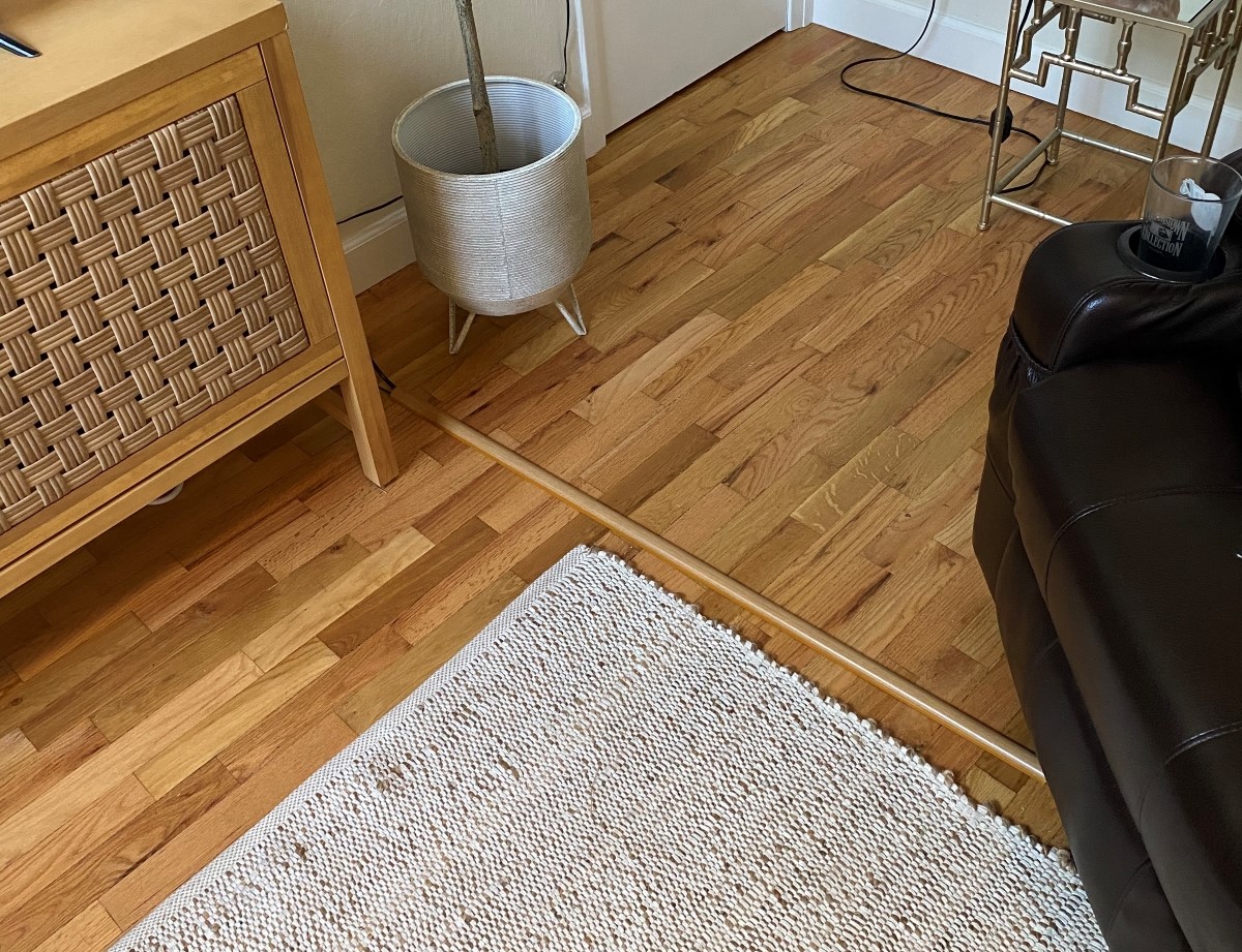 Brown cord cover hiding cables on a hardwood floor.