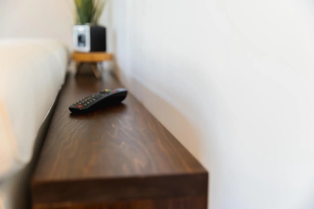 Narrow dark wood table behind a sofa, with a remote control and lamp on top.