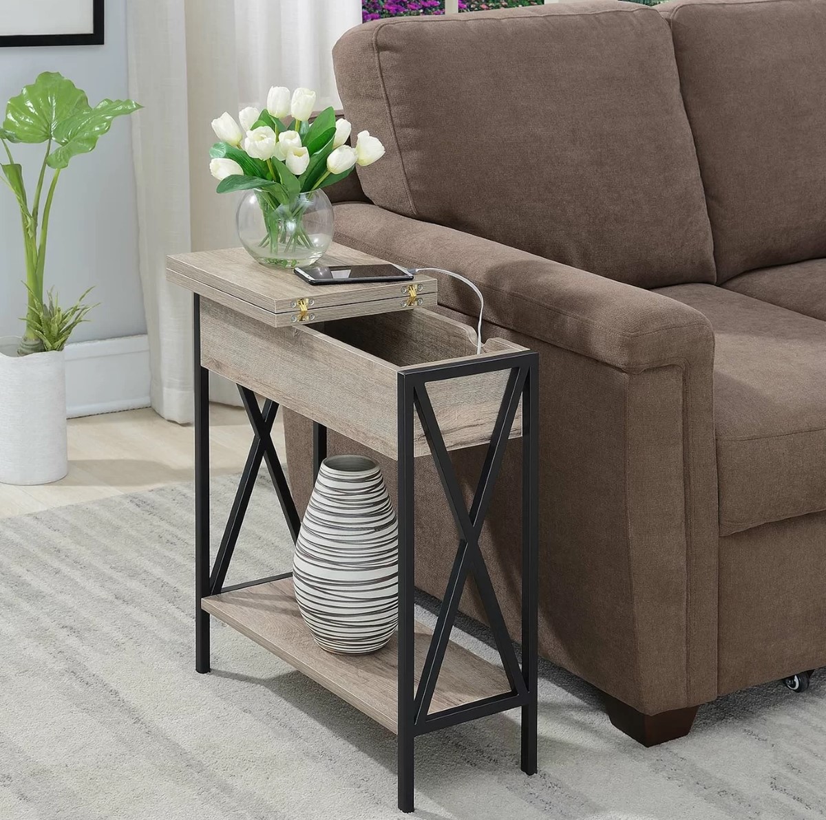 Narrow wood side table in the living room with a flip-back top next to a brown sofa.