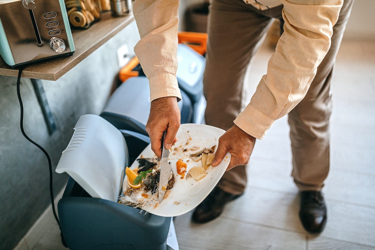 A man scraping leftover food scraps from a plate into a garbage can.