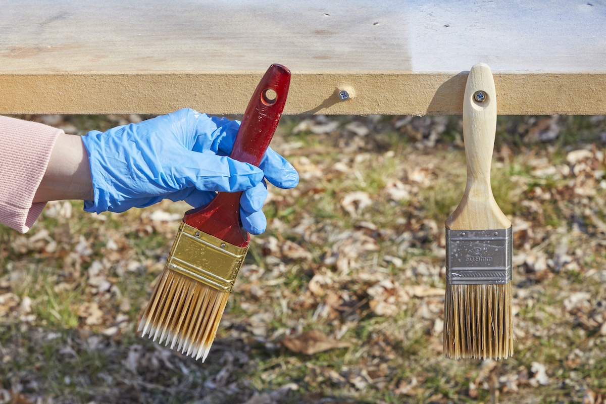 Woman hangs two paint brushes bristle-side down on a table outdoors.