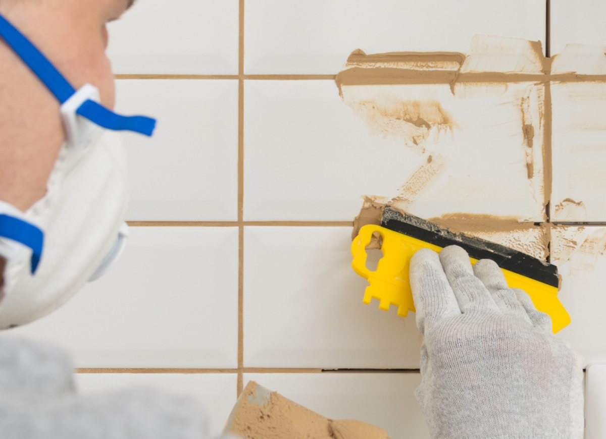 Master rubbing the seams on the laid white tiles on the wall, finishing work