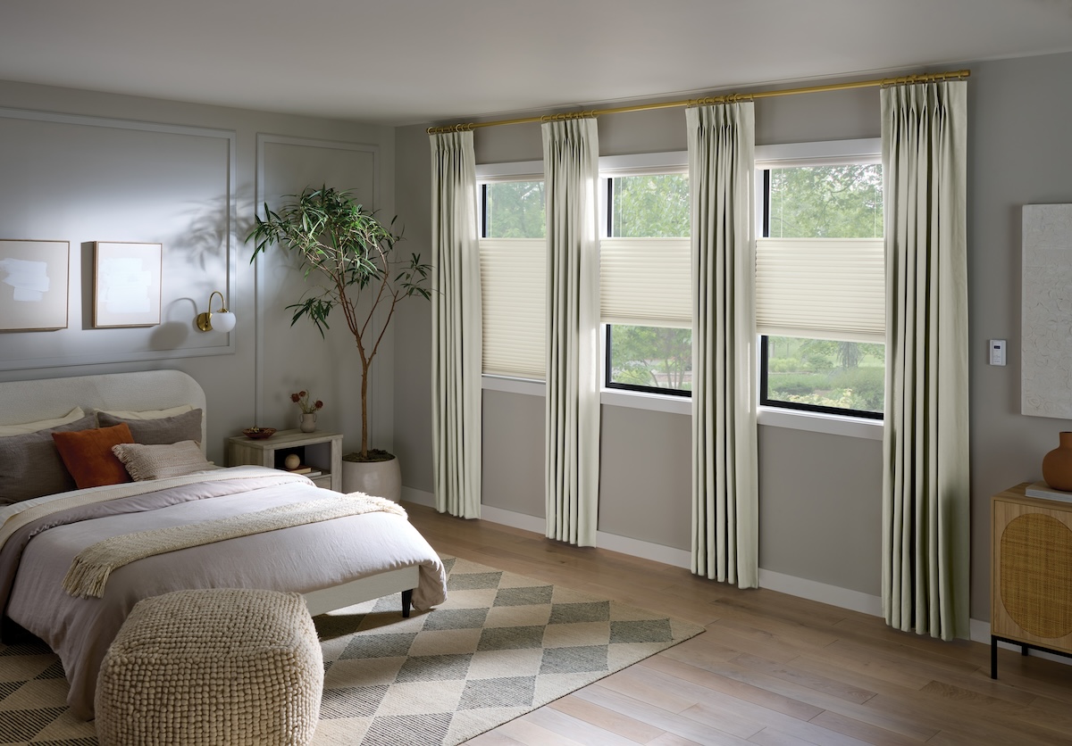 A bedroom with grey walls and large windows with both blinds and curtains dressing them.