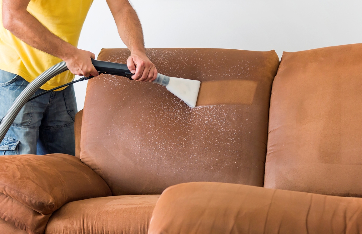 Person using vacuum to deep clean couch.