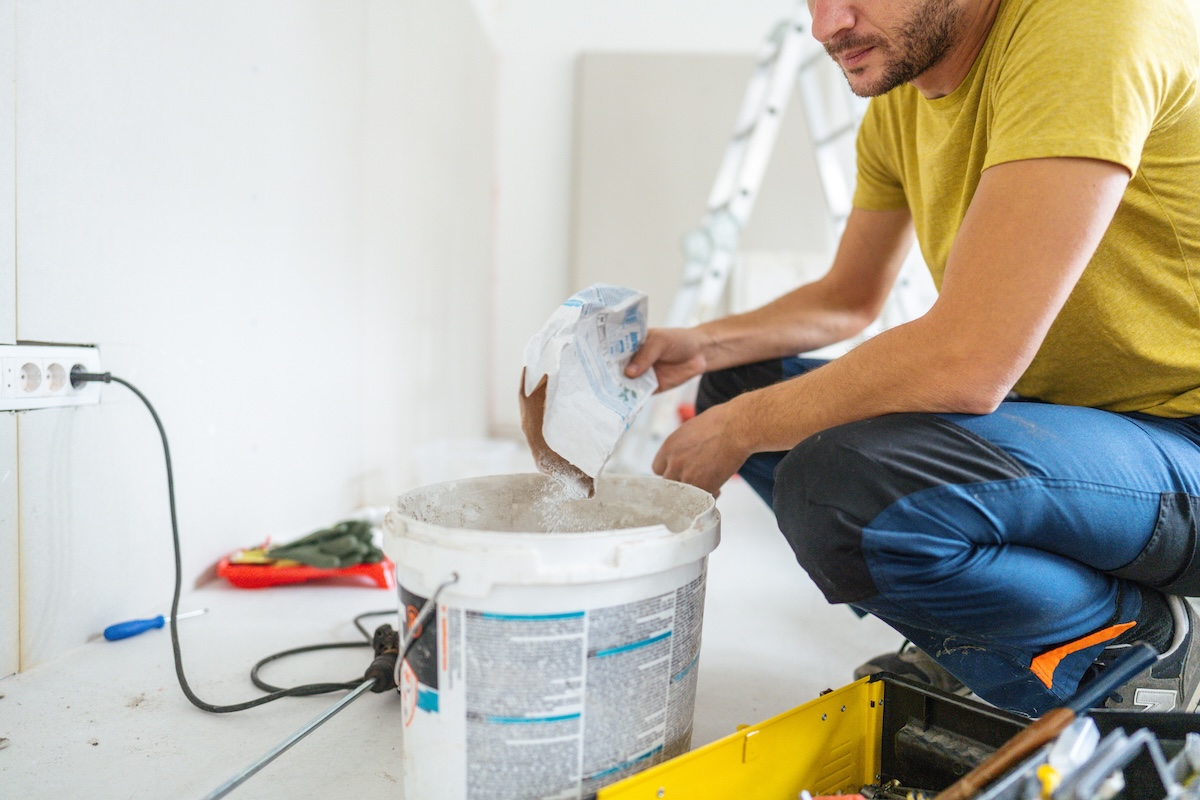 A man in a yellow shirt mixes drywall mud.