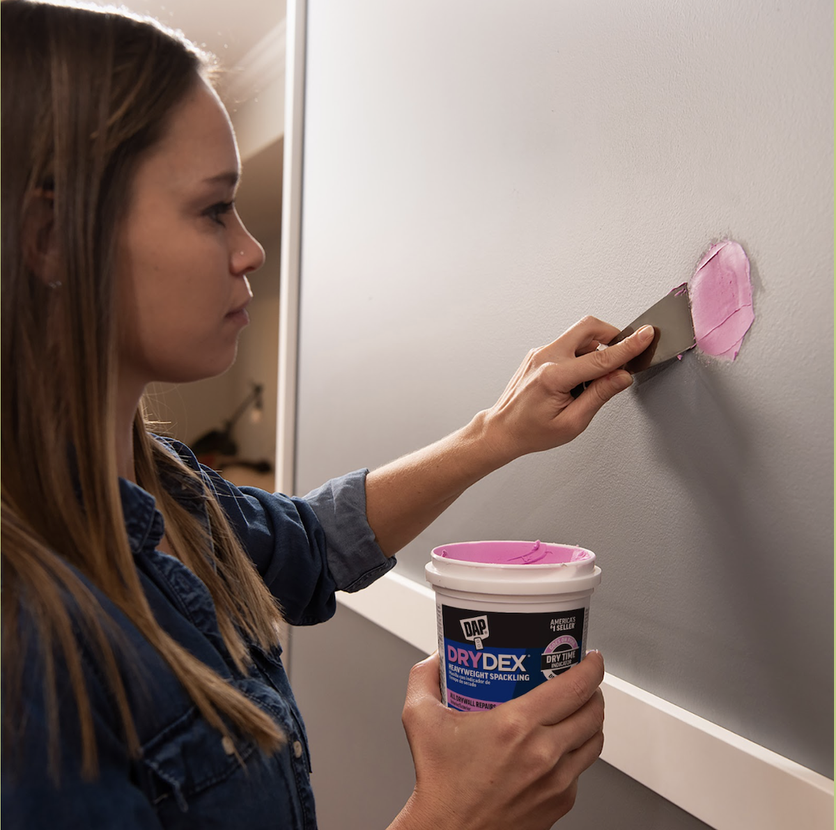 A young woman applies pink spackling to a grey wall.