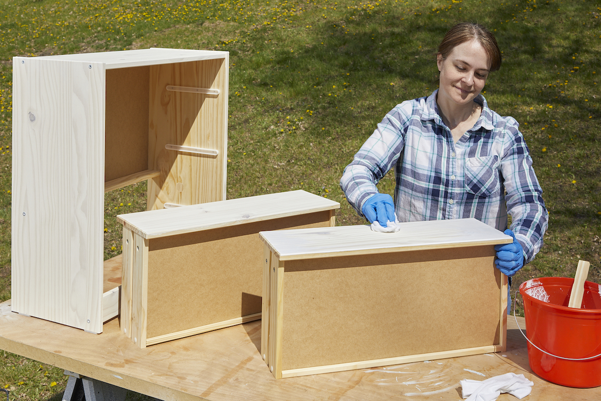 Woman whitewashes a wood dresser with two drawers removed.