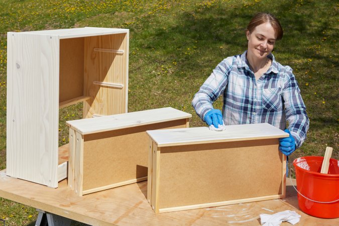 Woman whitewashes a wood dresser with two drawers removed.