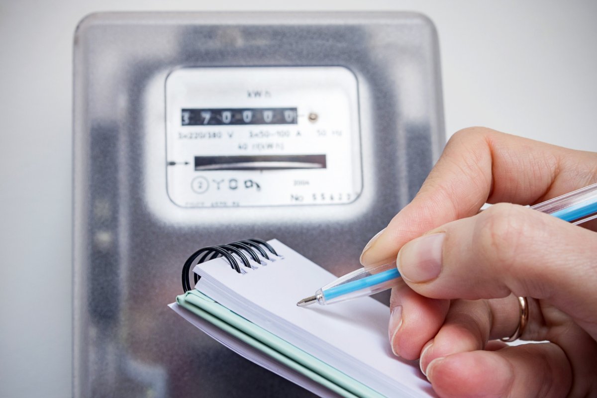 Person holds a pad of paper and a pencil in front of an electrical meter.