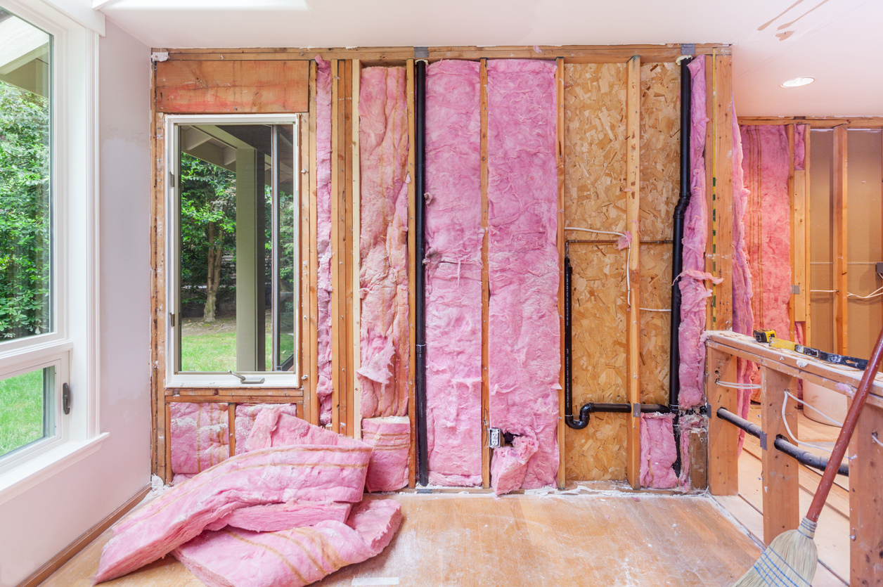 Interior room of a home with no sheetrock on walls, and exposed insulation and studs.