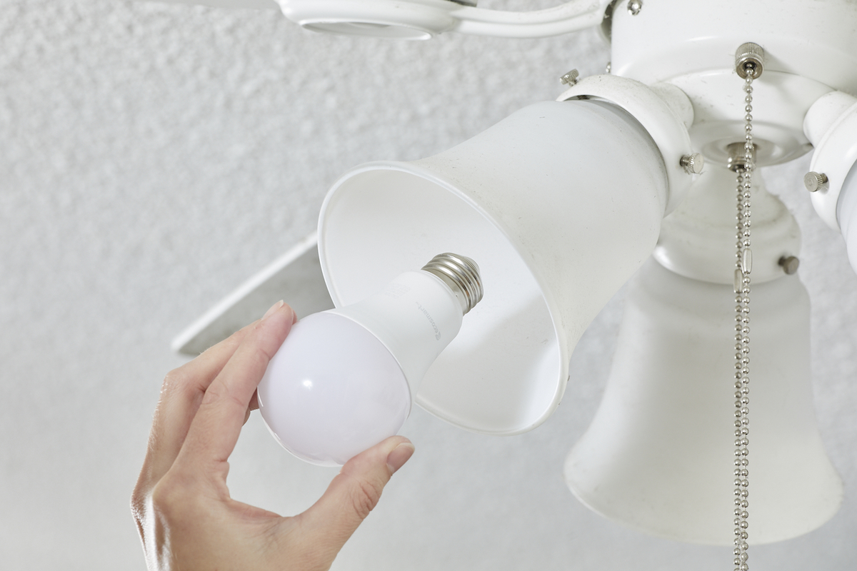 Woman replaces light bulbs in a white ceiling fan light fixture.