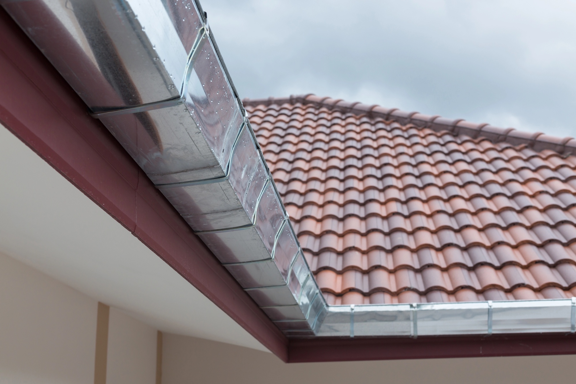 Aluminum box gutters meet at an inside miter on the corner of a tiled roof's eaves.