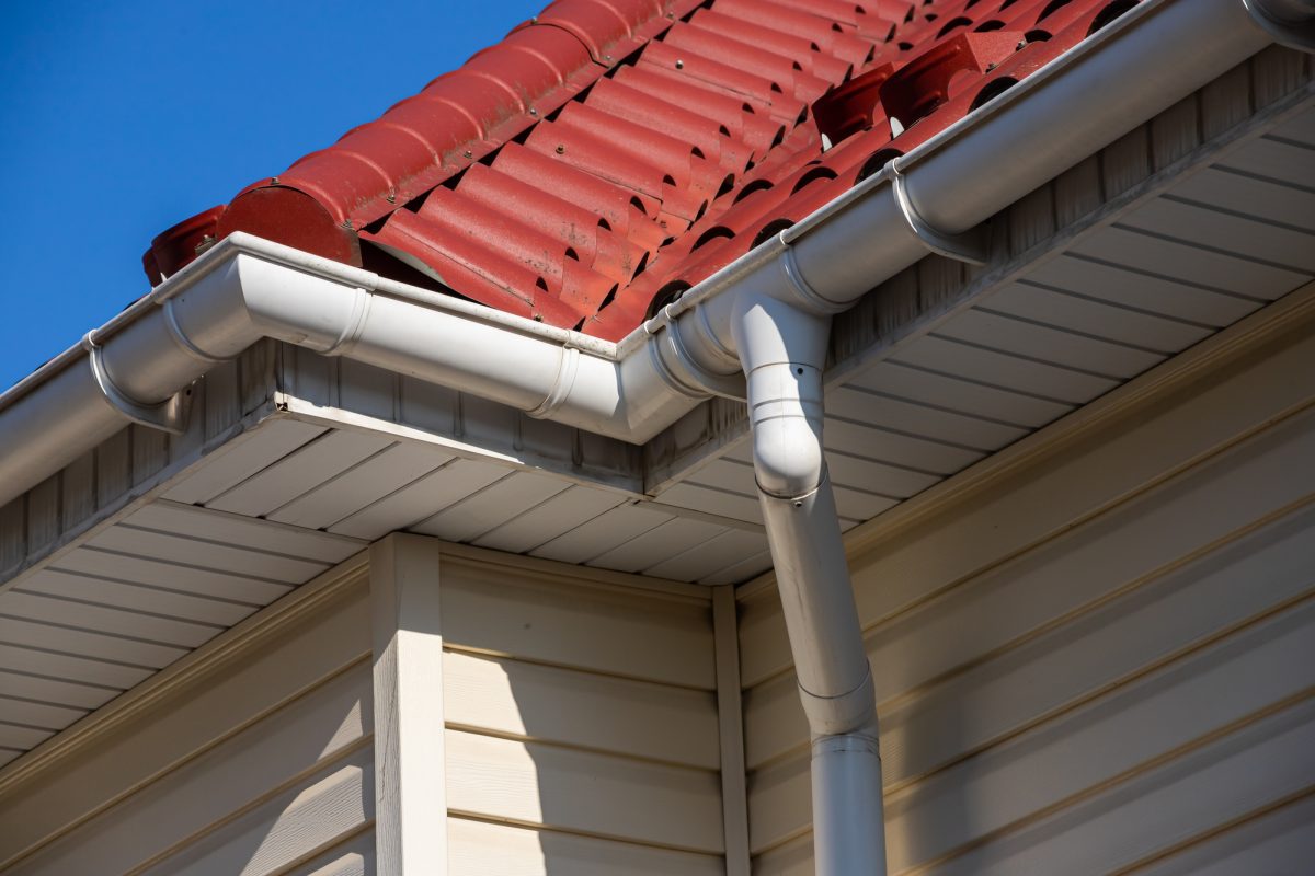 A new-construction home has a bright red metal-shingled roof and white half-round gutters.