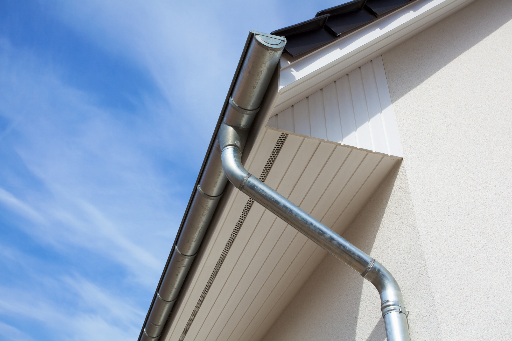 Steel gutters and a steel downspout add a metallic touch to a home with a white and black exterior.