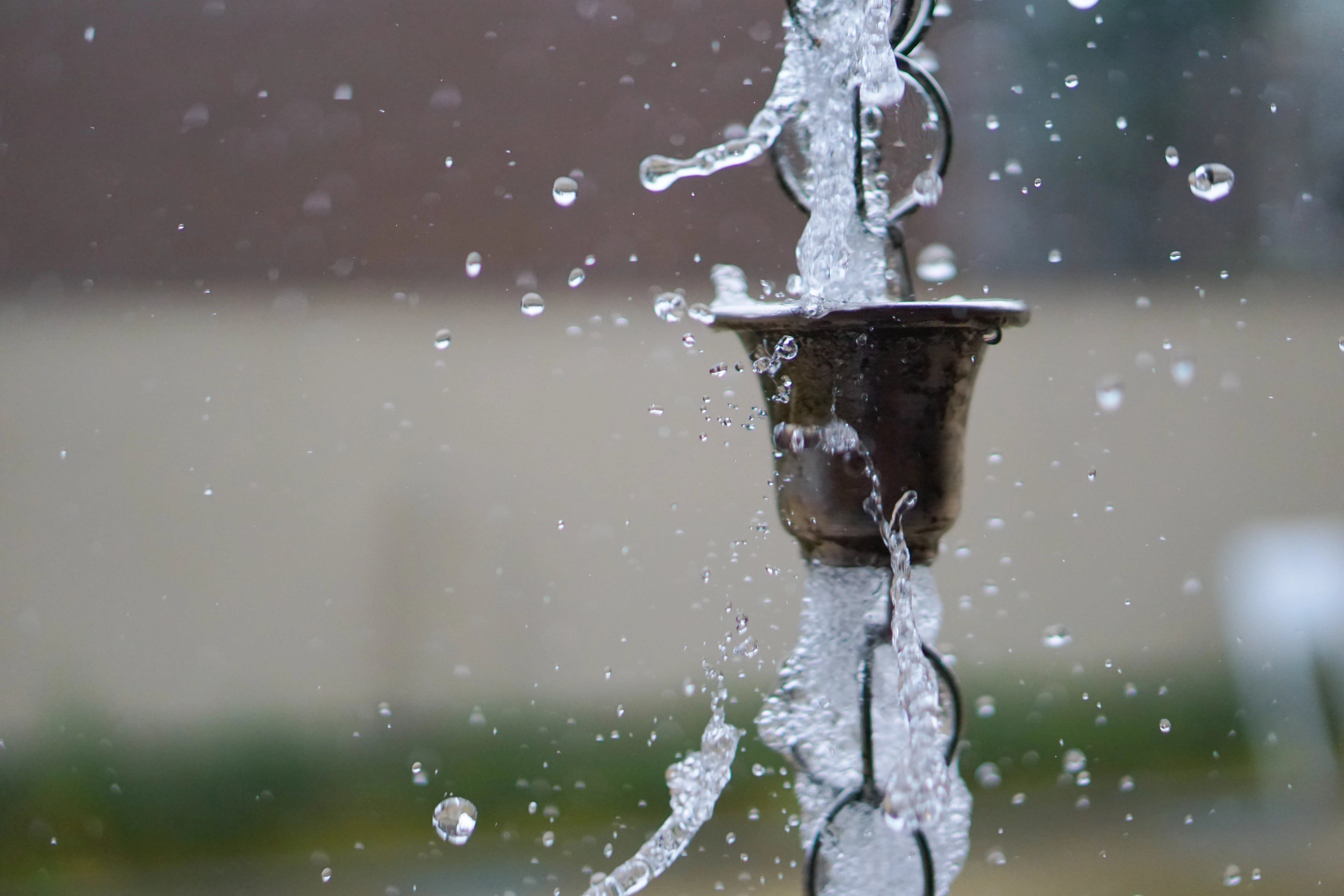 Water splashes through a rain chain hanging from a gutter. 