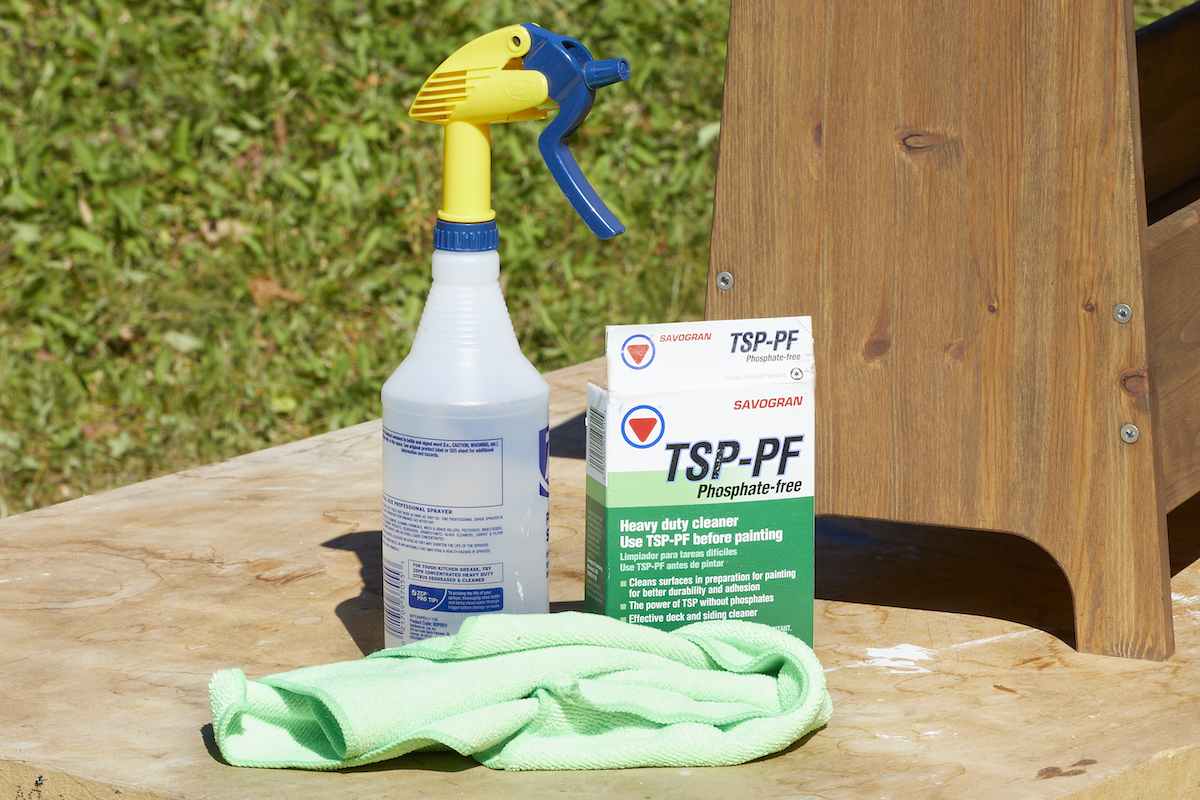 TSP, a spray bottle, and a rag next to a stained wooden bench.