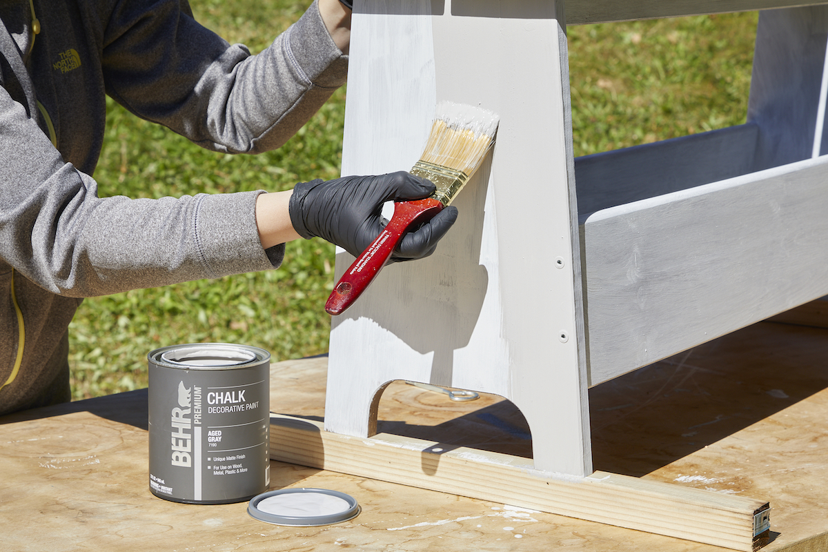 Woman paints chalk paint over primer on a wood bench.