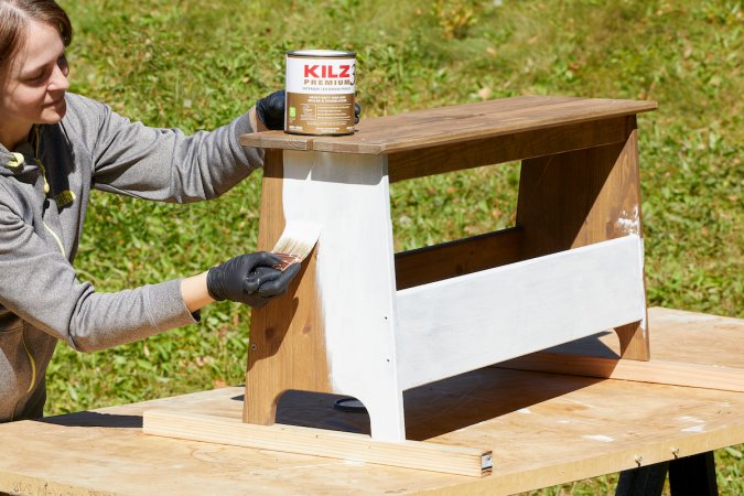 Woman paints primer over a stained wood bench.